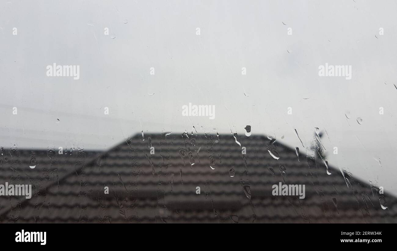 Fenêtre en gouttes de pluie. L'eau tombe sur le verre. Toit sur l'arrière-plan Banque D'Images