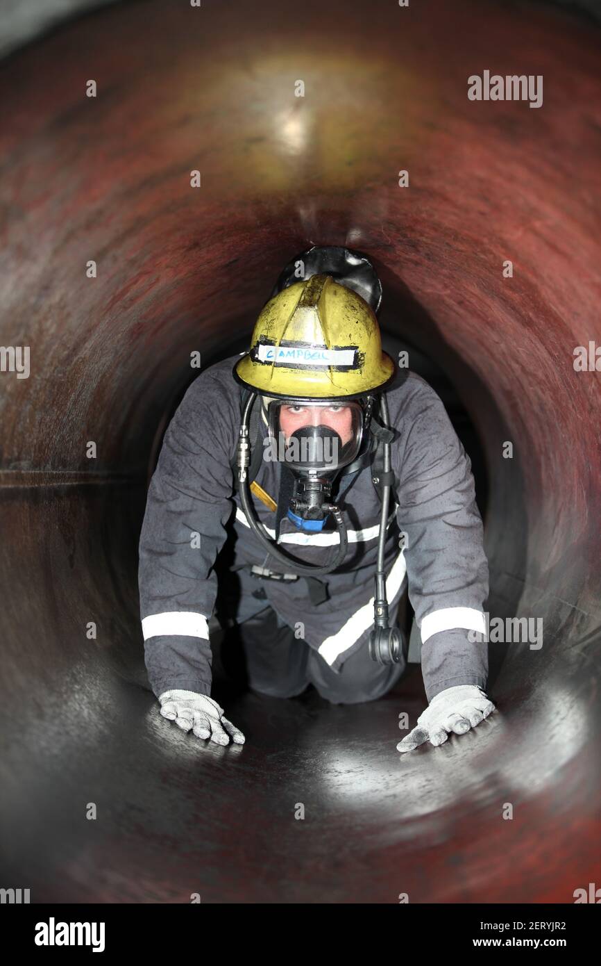 Un stagiaire en incendie portant un appareil respiratoire (BA) en cours de formation en espace confiné dans un tuyau Banque D'Images