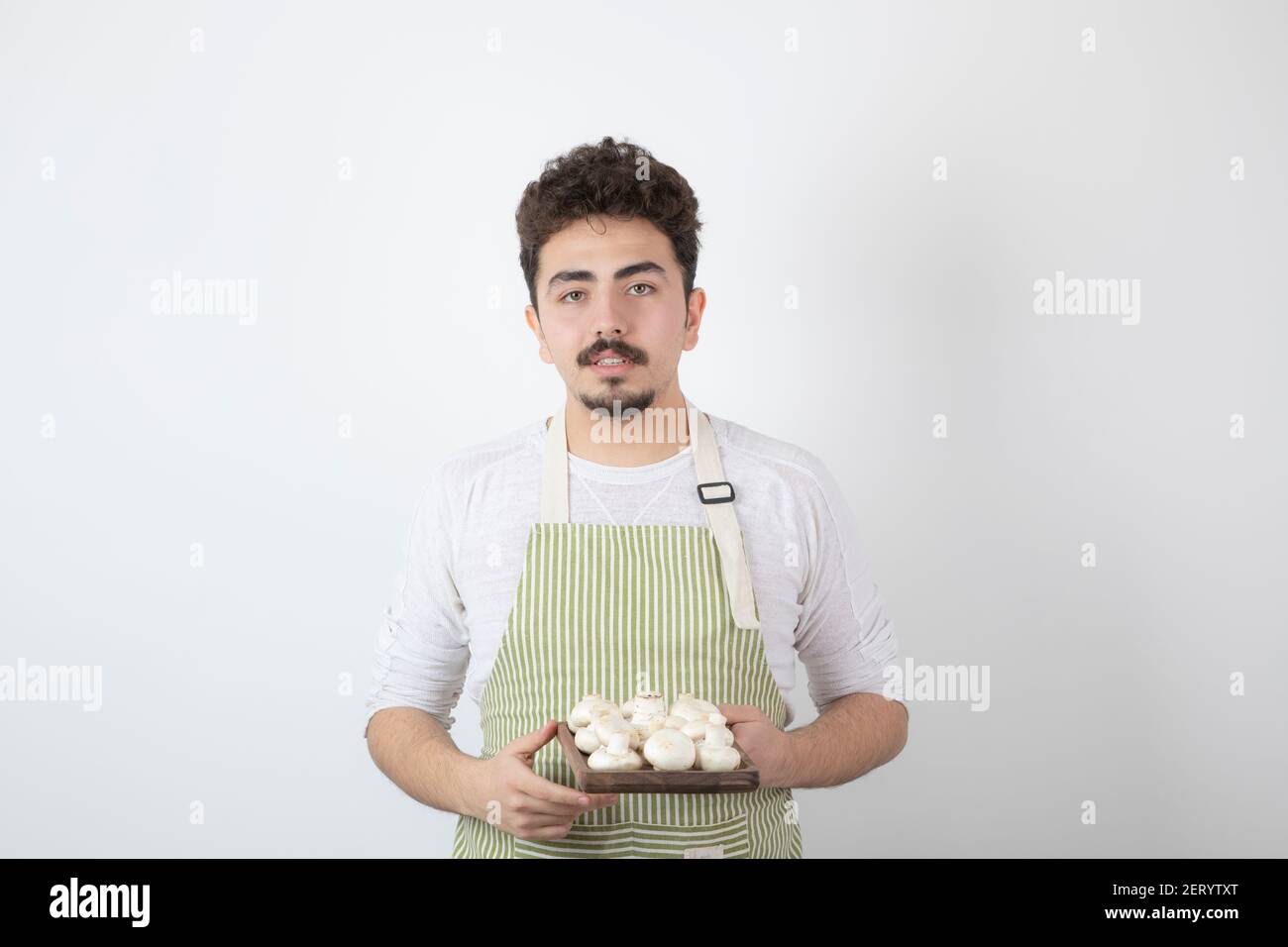 Portrait d'un jeune homme cuisinier tenant des champignons crus sur fond blanc. Photo de haute qualité Banque D'Images
