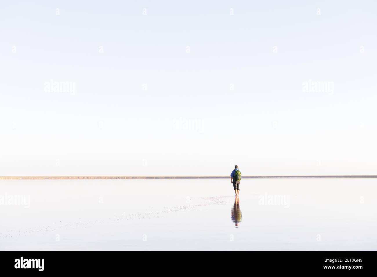 Paysage minimaliste tranquille avec homme solitaire en bleu jacré avec eau calme avec horizon avec ciel clair. Photographie de paysage minimale Banque D'Images