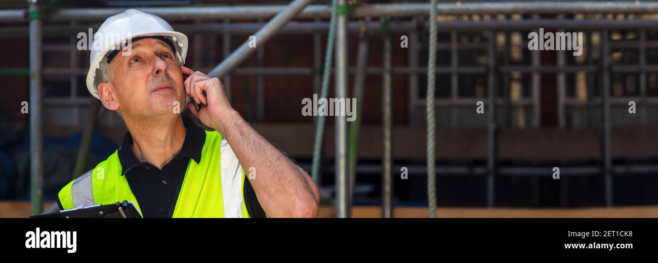 Panorama homme réfléchi contremaître de constructeur, ouvrier de construction, entrepreneur ou architecte sur le chantier de construction tenant la planchette noire et parlant sur son cel Banque D'Images