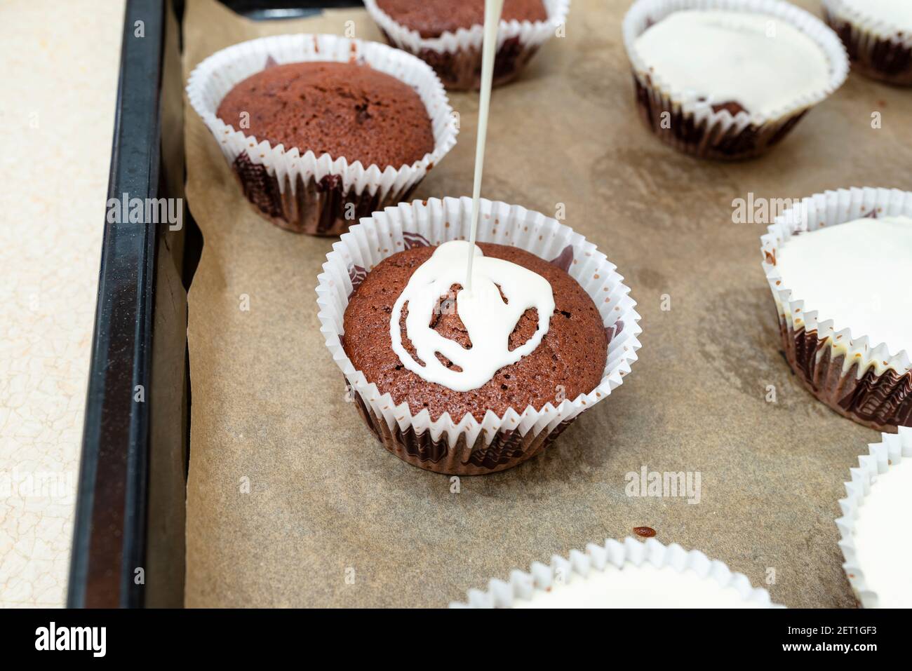 Gâteau au muffin brun chocolat enveloppé de papier blanc et recouvert de  glaçage blanc, cuit au four, allongé sur du papier de cuisson Photo Stock -  Alamy