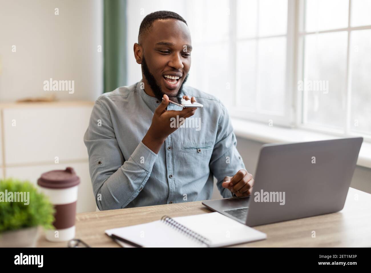Homme d'affaires afro-américain parlant en tenant son smartphone près de la bouche sur le lieu de travail Banque D'Images