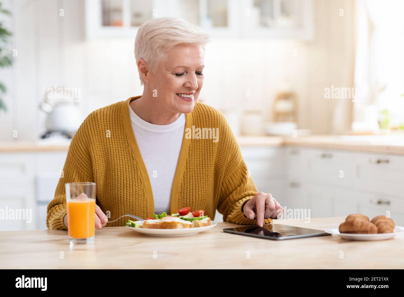 Femme âgée souriante mangeant des aliments sains et utilisant une tablette numérique Banque D'Images