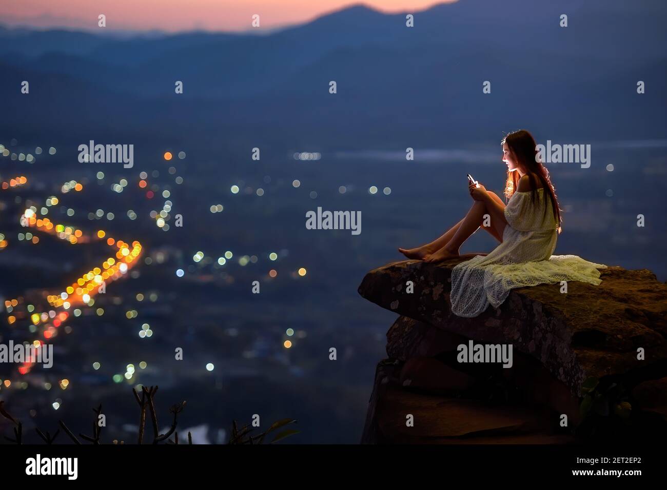Femme assise sur une corniche au-dessus de la ville à l'aide d'un téléphone portable, Thaïlande Banque D'Images