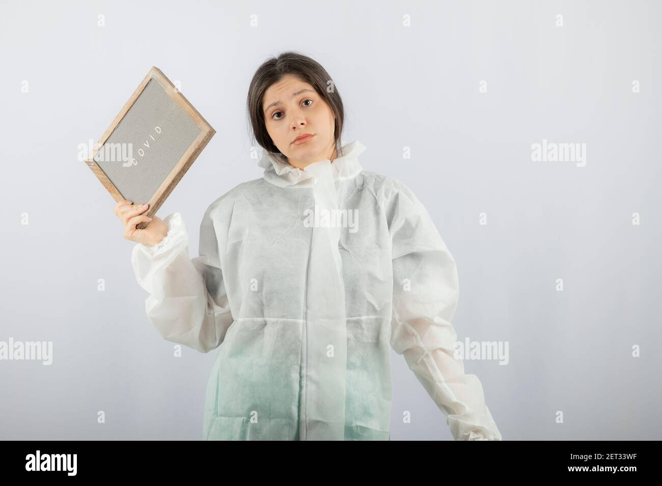 Photo d'un modèle de jeune fille en blouse de laboratoire défensive sur un mur blanc Banque D'Images