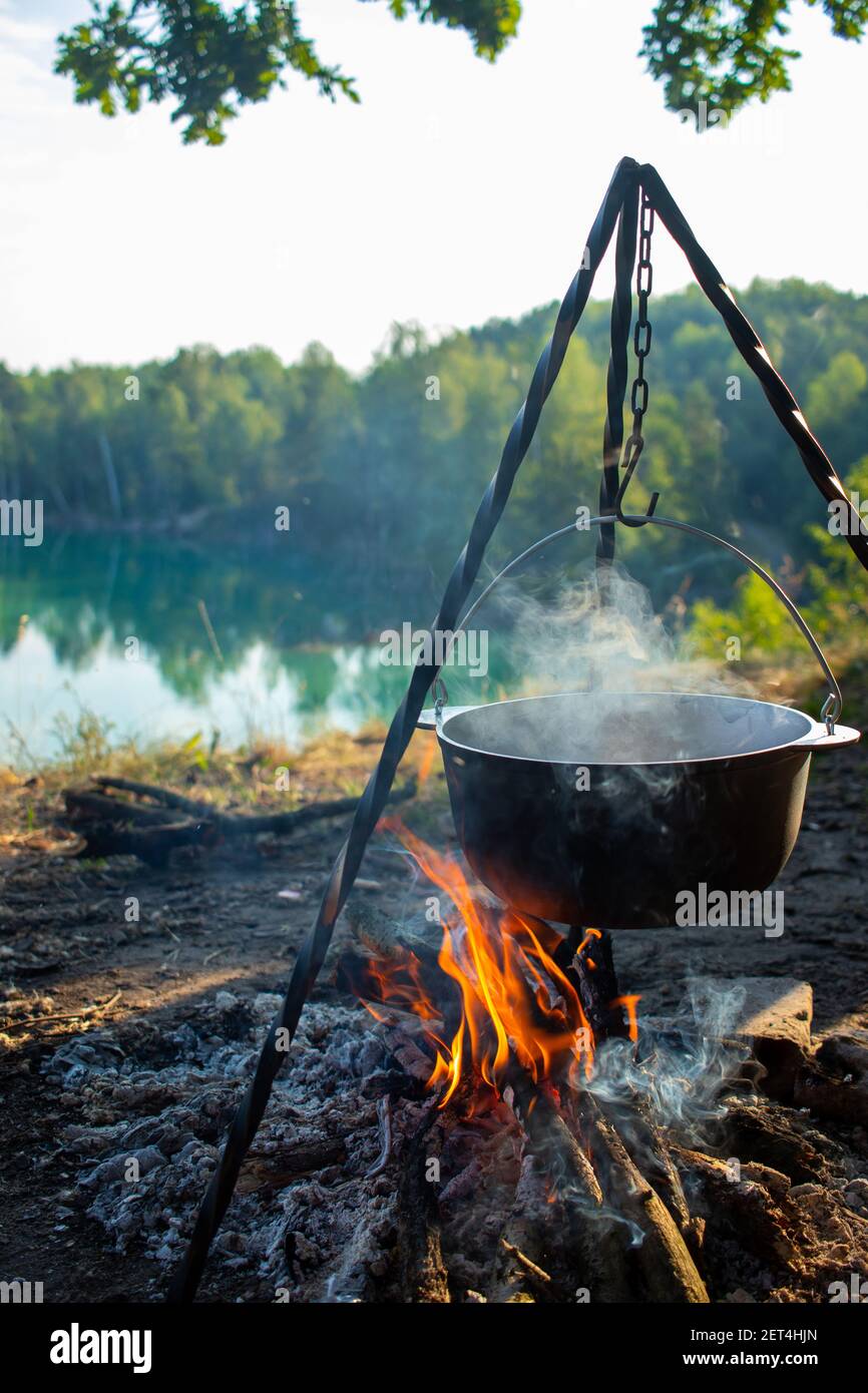 Cuisiner au piquet pendant les déplacements. Trépied avec un chapeau de melon sur un feu sur le fond d'un lac près de la forêt. Voyages conceptuels, trekking et Banque D'Images