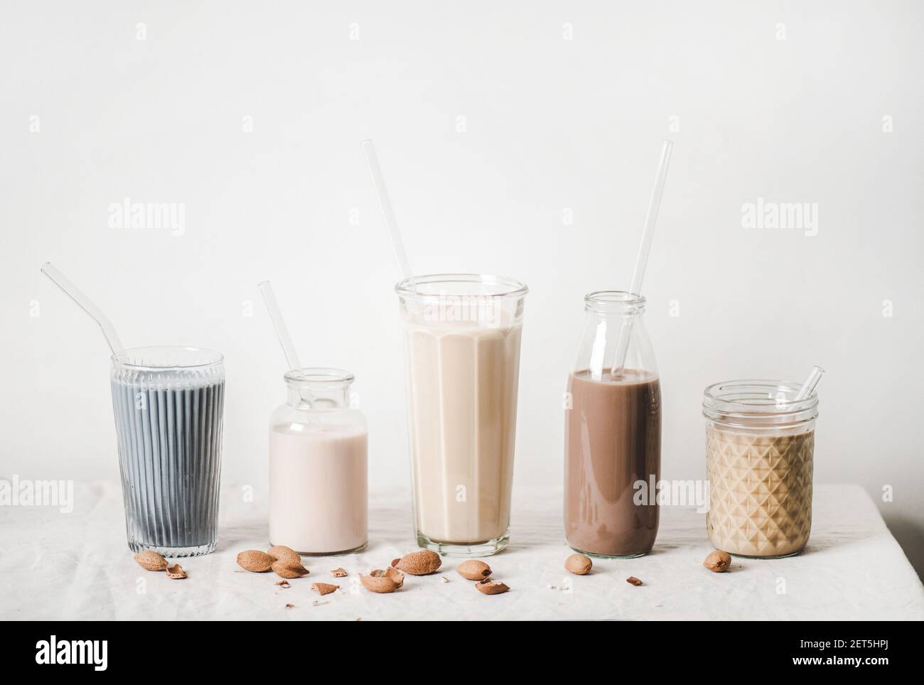 Lait sans lait aux amandes avec matcha bleu, baies, café, cannelle, cacao en bouteilles et verres de suite et ingrédients à base de noix sur nappe, fond blanc, espace de copie. Végétalien, nourriture alcaline Banque D'Images