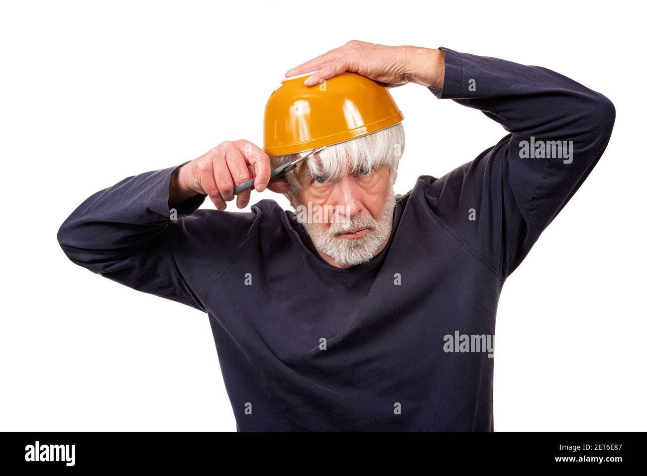 Plan horizontal d'un vieil homme qui se donne une coupe de cheveux à l'aide d'un bol jaune sur sa tête pendant la pandémie. Arrière-plan blanc. Banque D'Images