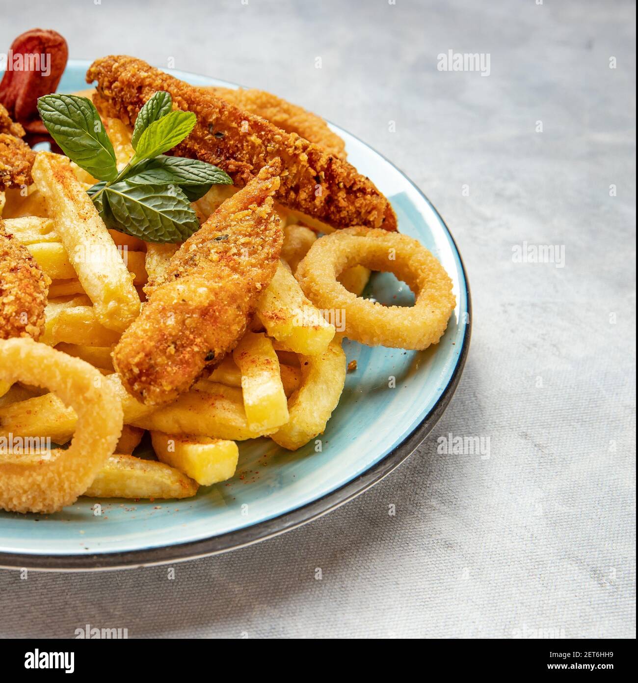 Frites, rondelles d'oignon et ailes de poulet dans une assiette bleue sur fond bleu-gris Banque D'Images