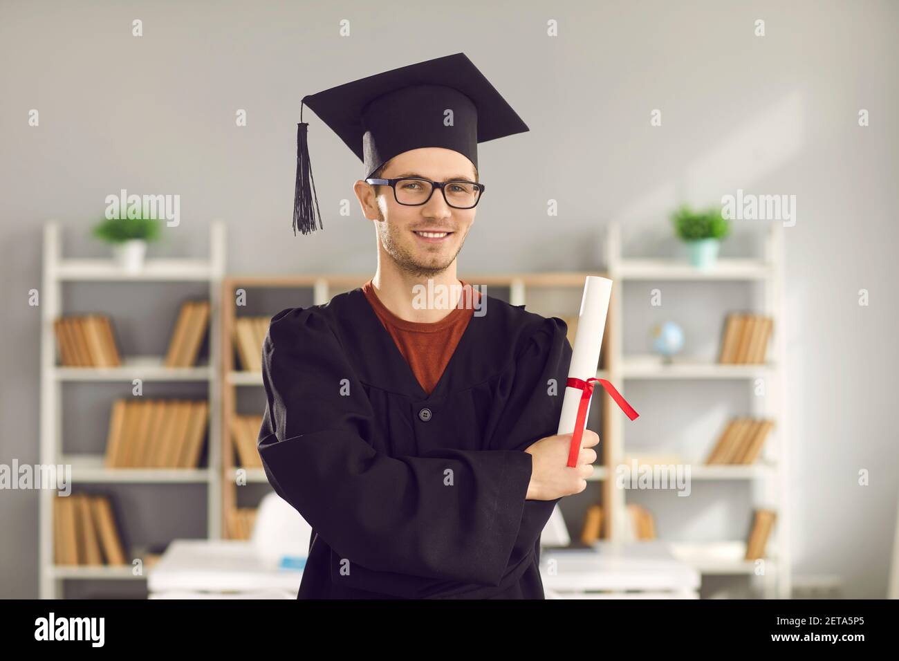 Heureux diplômé de l'université debout en classe, titulaire d'un diplôme et souriant à la caméra Banque D'Images