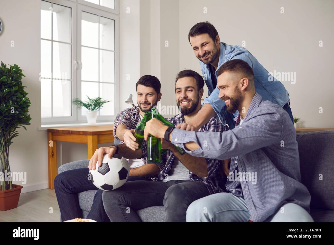 Des hommes souriants et excités se sont embués de bouteilles avec de la bière pendant le visionnement match de football à la télévision Banque D'Images