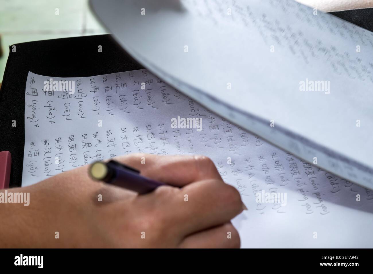 Des caractères chinois sont écrits sur des feuilles de papier blanches par une main humaine avec un crayon propulsant Banque D'Images
