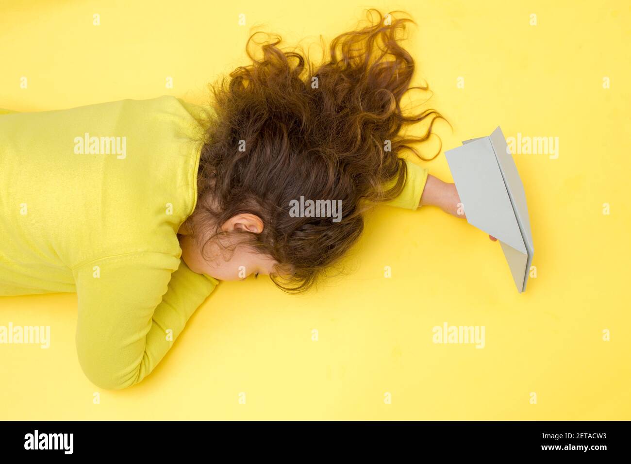 Fille endormi à la main avec un avion en papier gris sur fond jaune. Voyage créatif, concept de vacances pendant Covid-19 dans la couleur tendance 2021 Banque D'Images