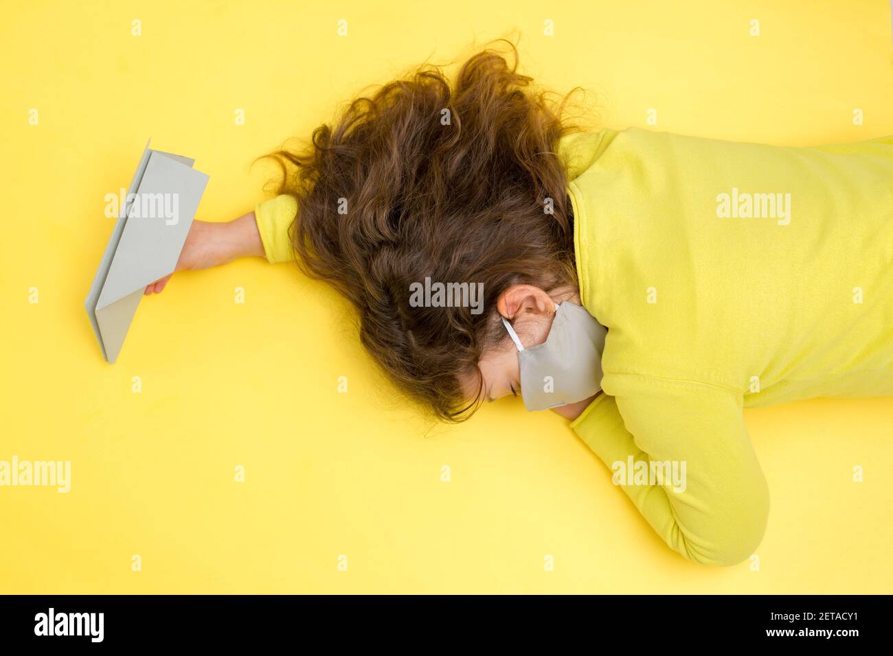 Fille dormant dans un masque gris protecteur en main avec un avion en papier gris sur un fond jaune. Creative Travel Covid-19, concept de vacances dans Banque D'Images