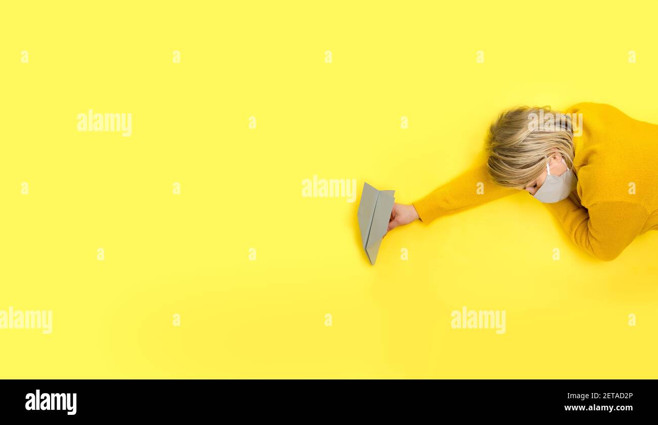 Femme dormant dans masque de protection gris en main avec avion en papier gris sur fond jaune. Concept de voyage Covid-19 créatif dans une couleur tendance Banque D'Images