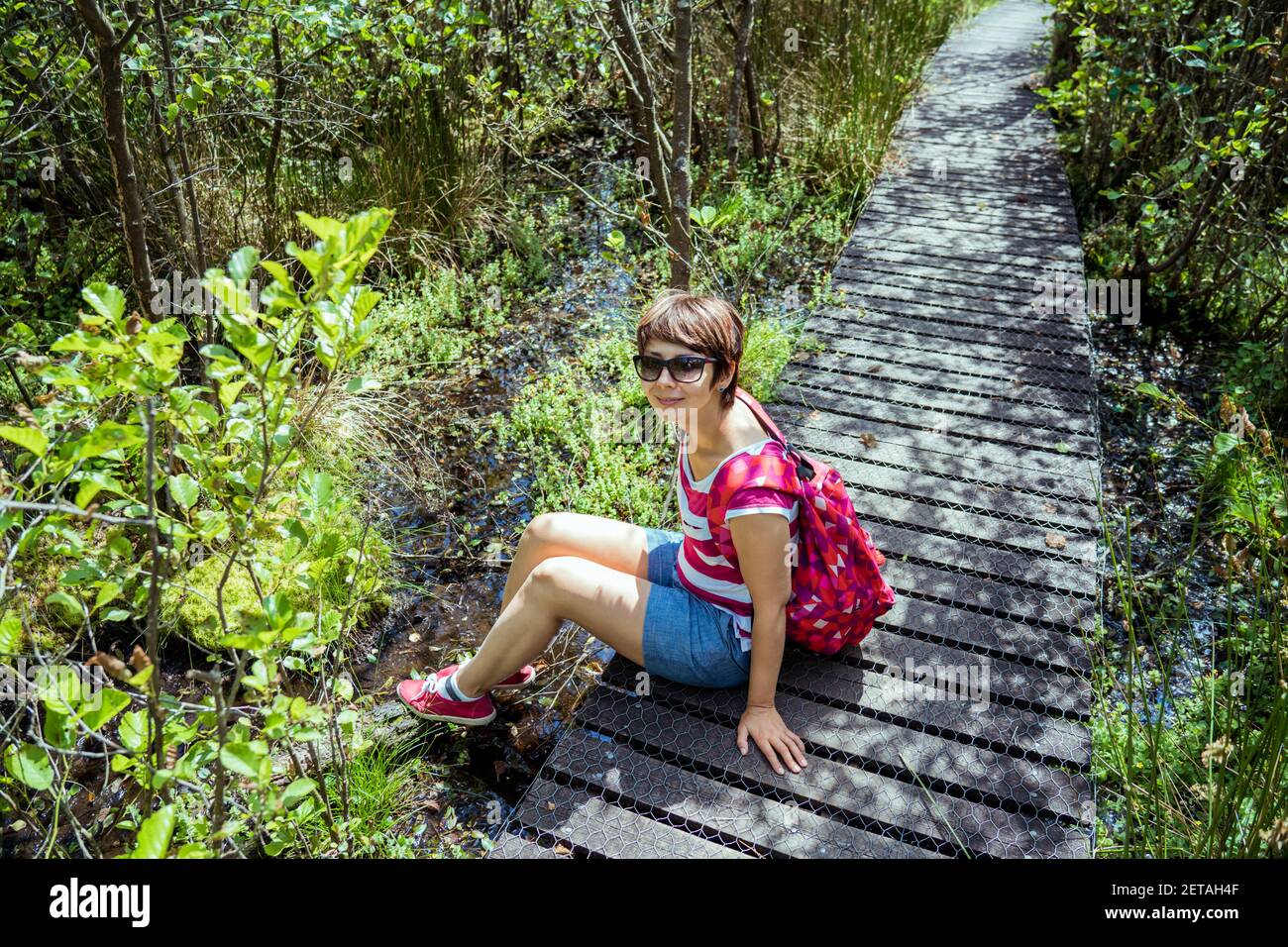 Une femme avec sac à dos assise sur le chemin en bois et se détendre après la randonnée dans la forêt d'été. Apprécier, unité avec la nature, détox numérique Banque D'Images