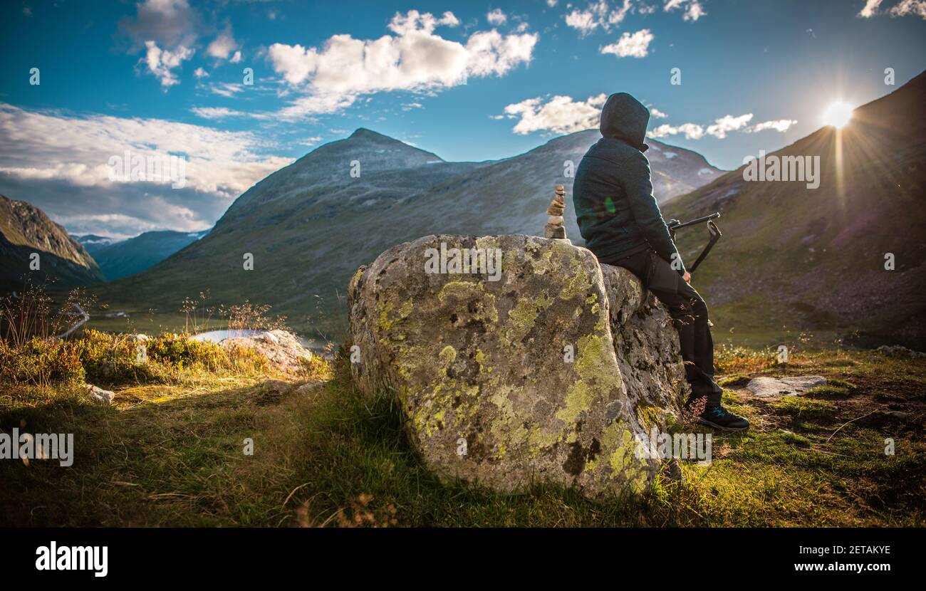 Un homme de randonnée alpin se repose pour regarder un coucher de soleil panoramique. Terrain de jeux Mountain Trail. Paysage norvégien. Banque D'Images