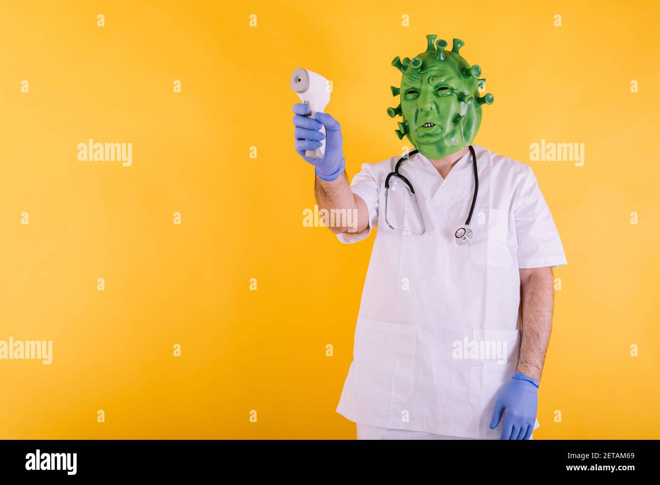 Médecin - infirmière en coronavirus déguisée portant un masque en latex - virus Covid-19 pointant avec un thermomètre électronique sur fond jaune. Coronavirus c Banque D'Images