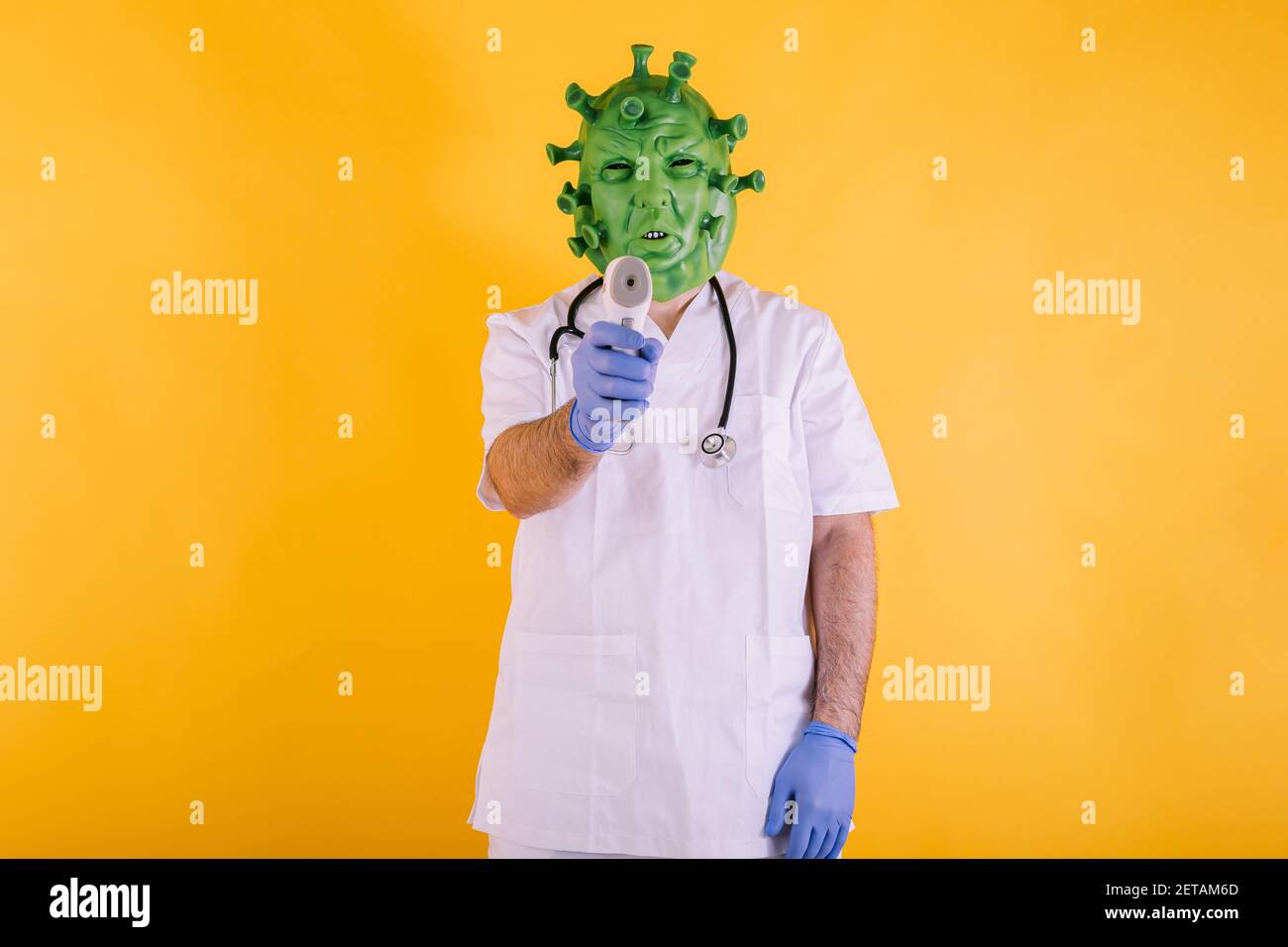 Médecin - infirmière en coronavirus déguisée portant un masque en latex - virus Covid-19 pointant avec un thermomètre électronique sur fond jaune. Coronavirus c Banque D'Images