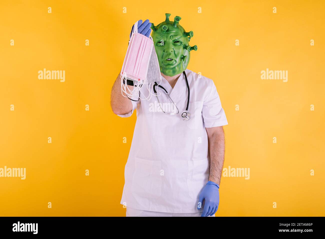 Médecin - infirmière déguisée comme coronavirus portant un masque de latex - virus Covid-19 avec des masques chirurgicaux dans sa main sur fond jaune. Concept de coronavirus Banque D'Images