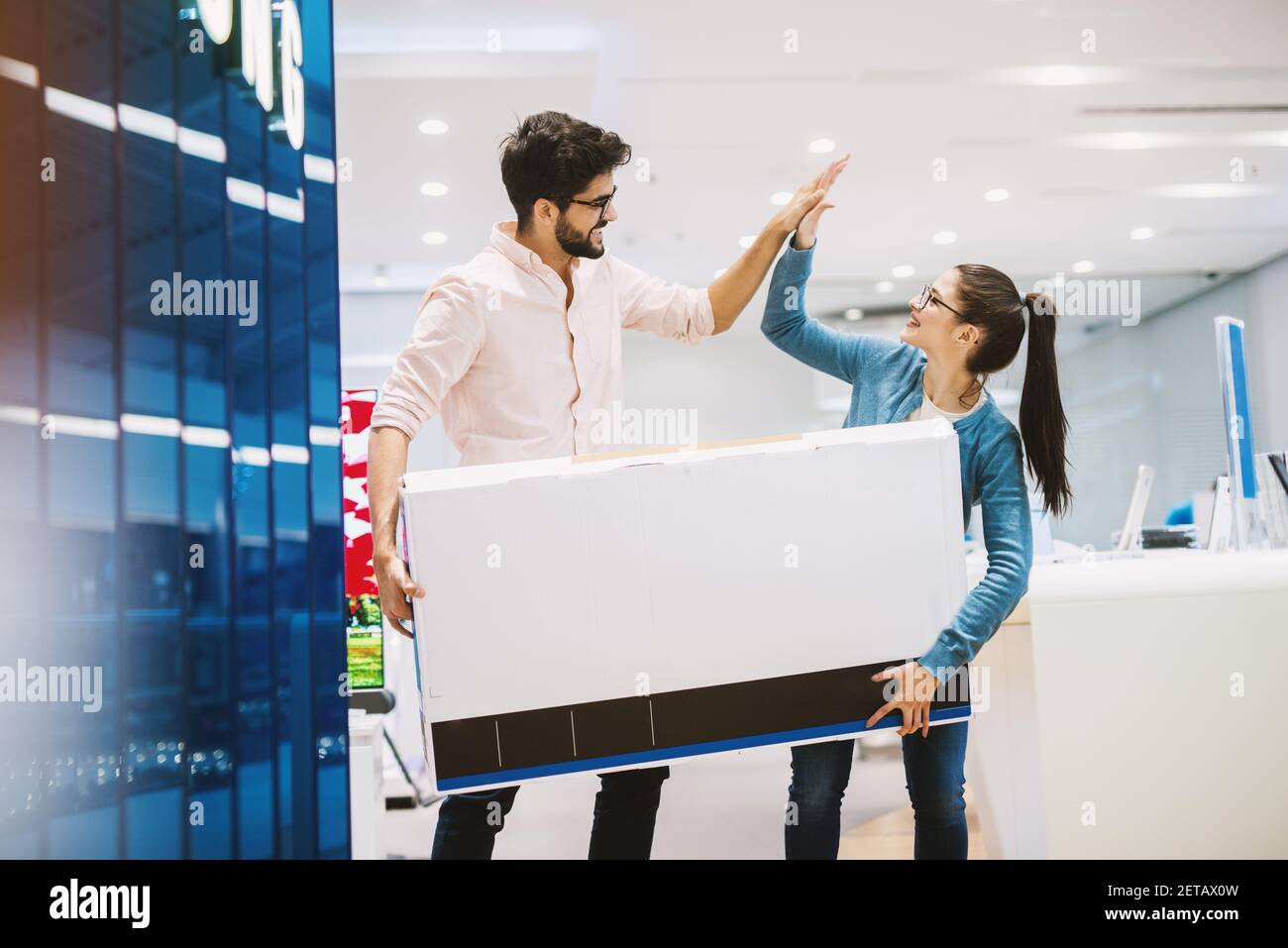 Un jeune beau couple amusant célèbre l'achat d'un nouveau téléviseur en haut-de-fiving. Banque D'Images