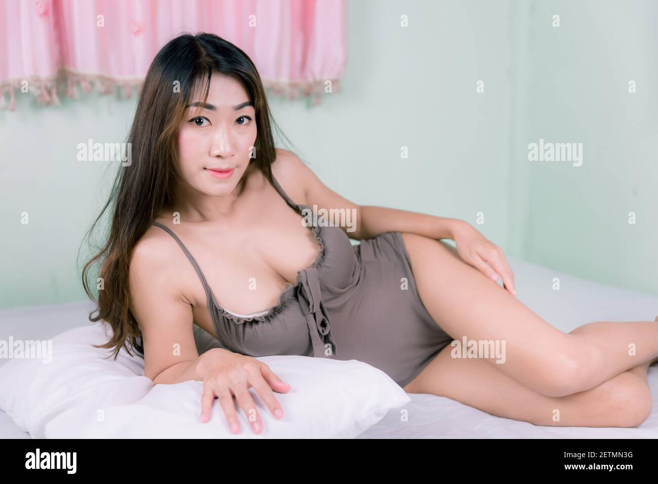 Sexy femme asiatique en pyjama marron sur un lit blanc Banque D'Images