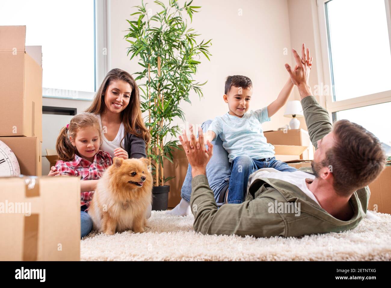 Maman, papa, leurs enfants et leur chien se déplaçant dans le nouvel appartement et s'amusant en faisant ainsi Banque D'Images