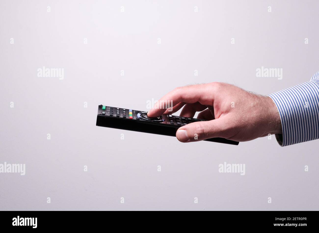 Main mâle tenant une télécommande de téléviseur appuyant sur les touches sur fond blanc, changeant de chaînes, concept de diffusion multimédia à domicile, studio intérieur Banque D'Images