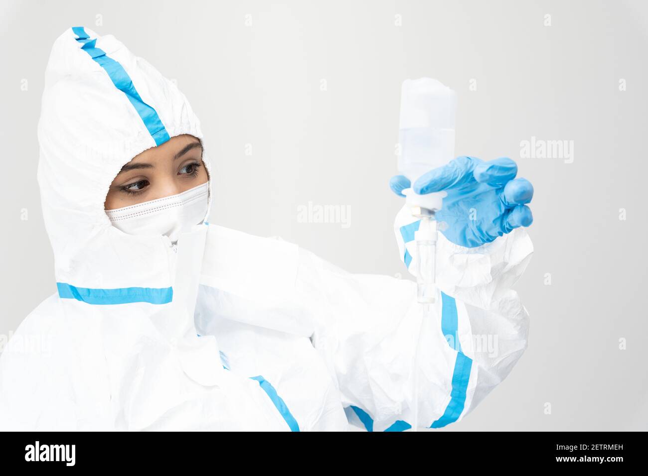 Femme médique en masque et costume de protection debout avec compte-gouttes dans la salle blanche en travaillant pendant l'épidémie de coronavirus Banque D'Images