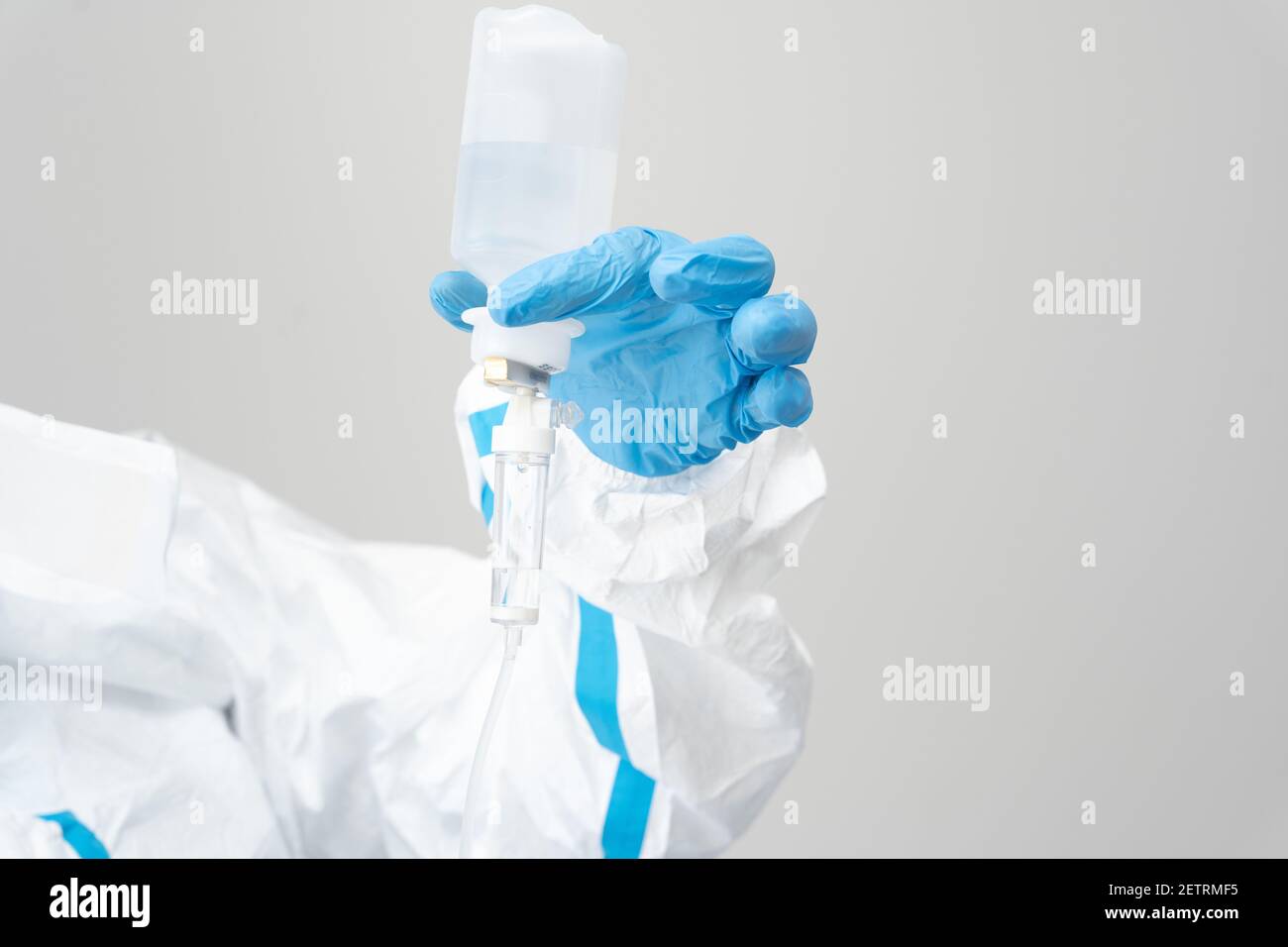 Crop médecin anonyme en costume de protection et gants en latex debout avec compte-gouttes dans la salle médicale pendant la pandémie du coronavirus Banque D'Images
