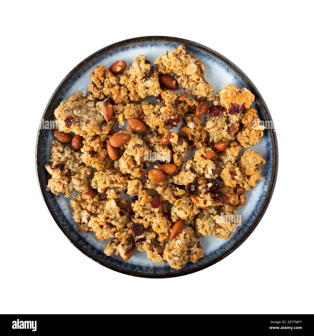 Vue de dessus d'un granola de grains entiers avec des fruits et des noix sur une assiette bleue sur un fond blanc. Banque D'Images