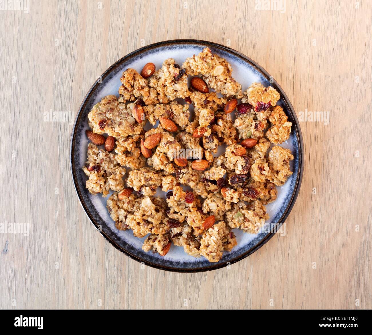 Vue de dessus d'un petit bol en verre rempli de céréales entières granola avec fruits et noix sur une assiette bleue au-dessus d'une table. Banque D'Images