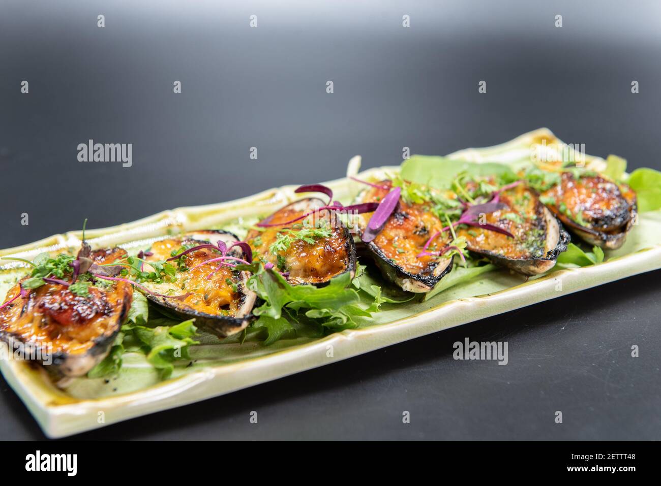 Hors-d'œuvre de moules cuites trempées dans une délicieuse sauce avec une belle présentation sur une assiette en bambou. Banque D'Images