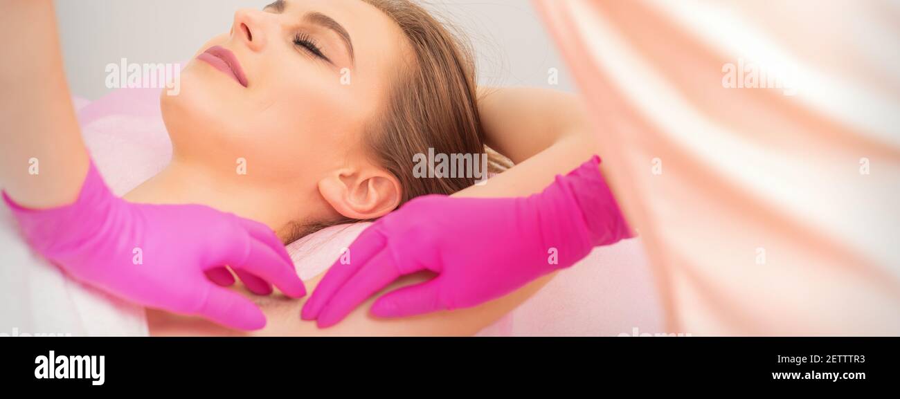 Jeune femme caucasienne recevant une aisselle à la cire par les mains dans  des gants d'esthéticienne en salon d'épilation Photo Stock - Alamy