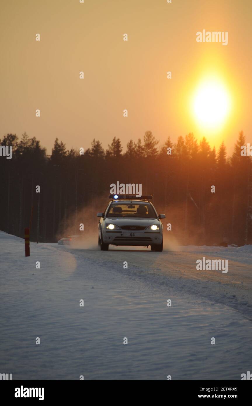 Un convoi de voitures bleues clignotantes de la police de la circulation finlandaise roule le long d'une route enneigée pendant les couchers de soleil d'hiver à Pieksamaki en Finlande. La police l'était Banque D'Images