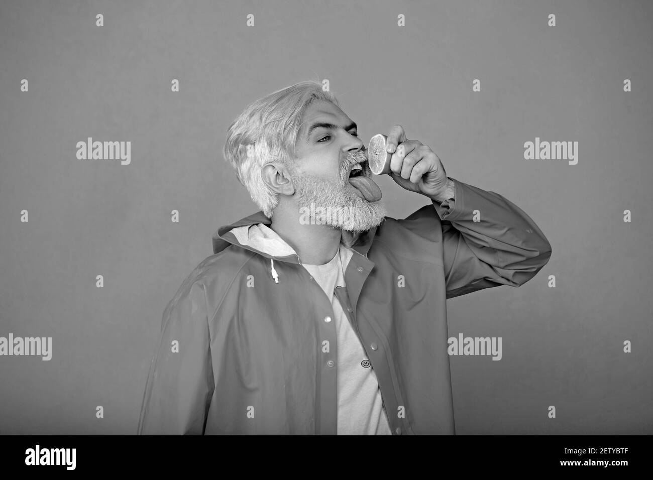 Un hipster barbu presse le citron aigre dans sa bouche, sur fond jaune. Banque D'Images