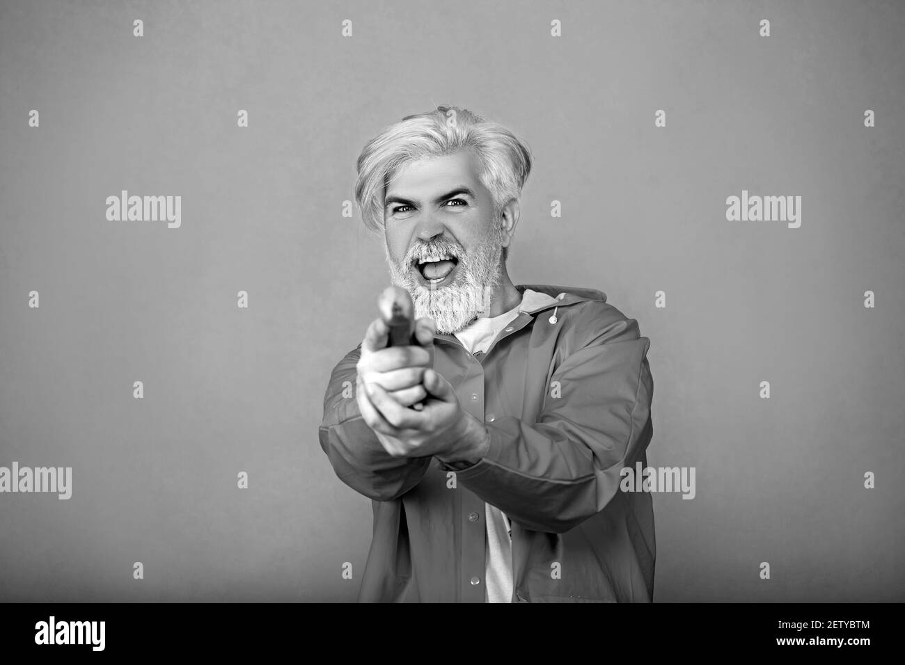 Portrait de jeune homme drôle debout sur fond jaune et utilisant la banane comme arme, regardant l'appareil photo avec le visage sérieux et jouant l'espion. Banque D'Images