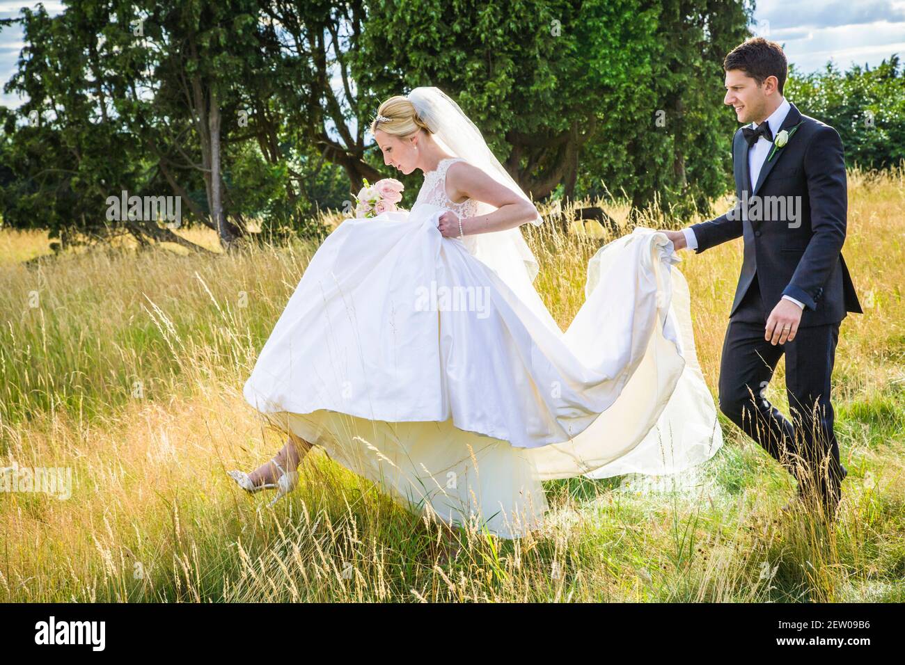 Bride et Bridegroom récemment-weds marchant à travers la longue herbe de Le domaine du manoir juste après qu'ils se sont mariés. Le marié est tenir le sentier Banque D'Images