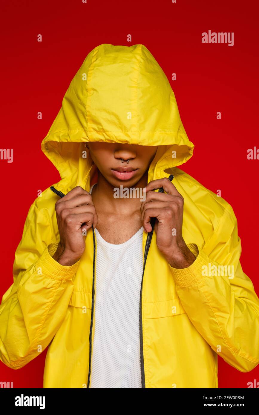 homme afro-américain élégant en veste de pluie jaune avec capuche isolé sur le rouge Banque D'Images