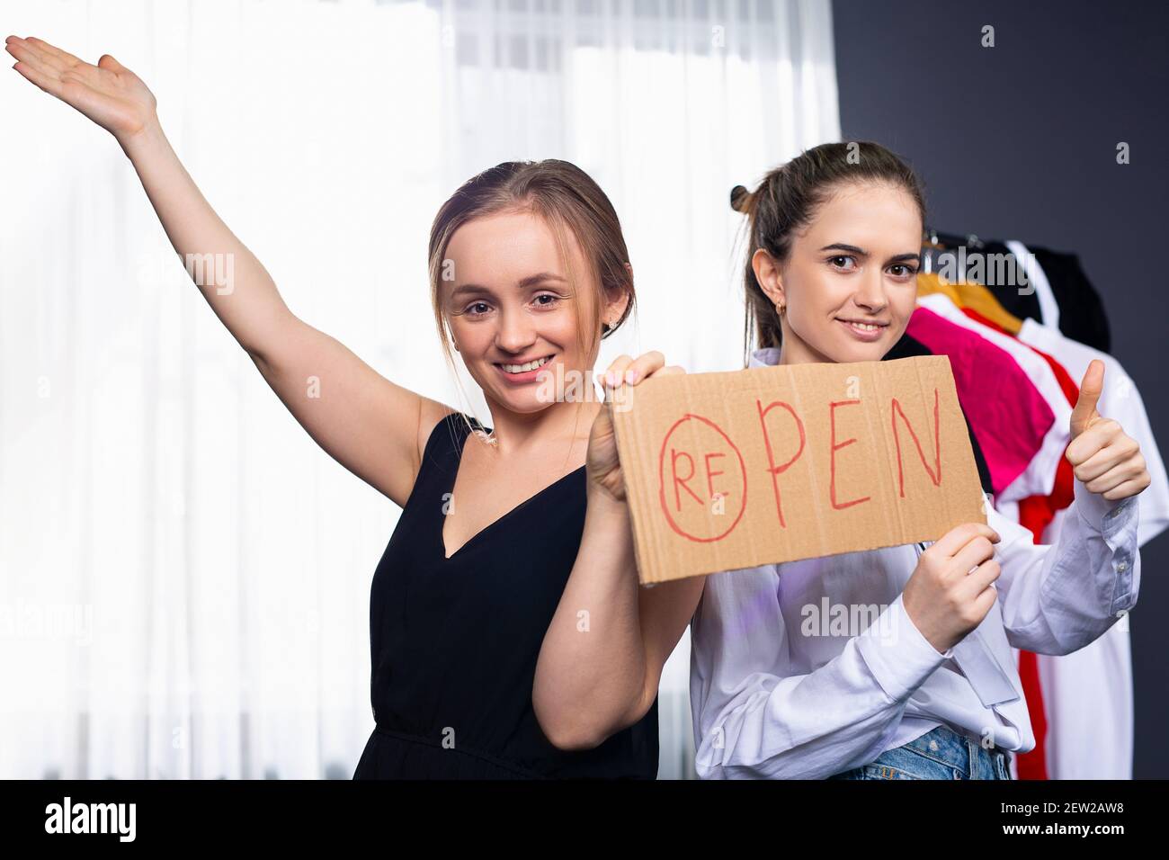 Deux femmes heureuses assises dans leur boutique et accrochant une AFFICHE OUVERTE sur la porte. Le propriétaire d'une petite entreprise qui met un panneau ouvert sur la porte en face de Banque D'Images