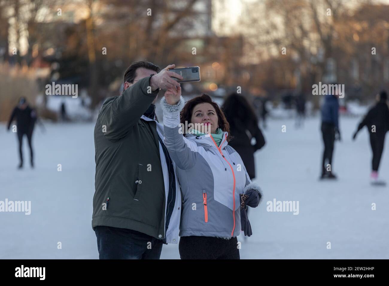 ZUTPHEN, PAYS-BAS - 13 févr. 2021: Couple regardant leur téléphone faire un selfie avec des gens sur la gelée au-dessus de la rivière Berkel pendant l'hiver dans la ba Banque D'Images