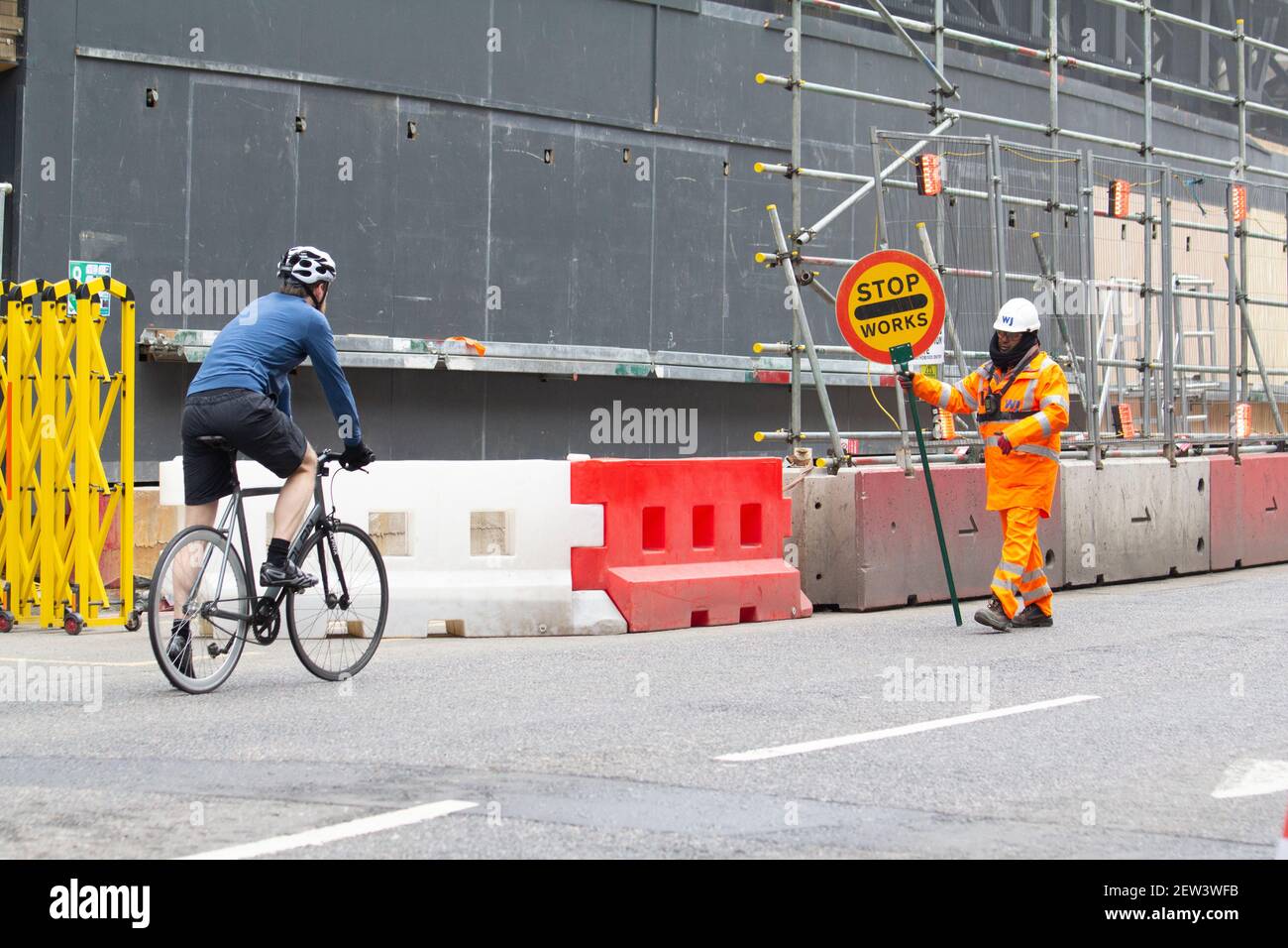 Un Traffic Marshall tient le panneau Stop pour arrêter un cycliste solitaire à venir City de Londres, pendant le coronavirus Covid-19 confinement pandémique Banque D'Images