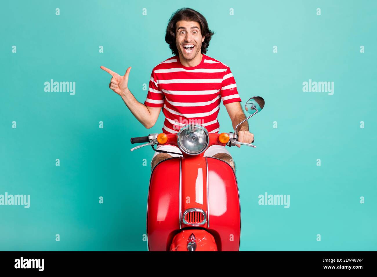 Portrait d'un beau gars gai stupéfié de l'équitation mobylette montrant la copie espace isolé sur fond vert clair turquoise Banque D'Images