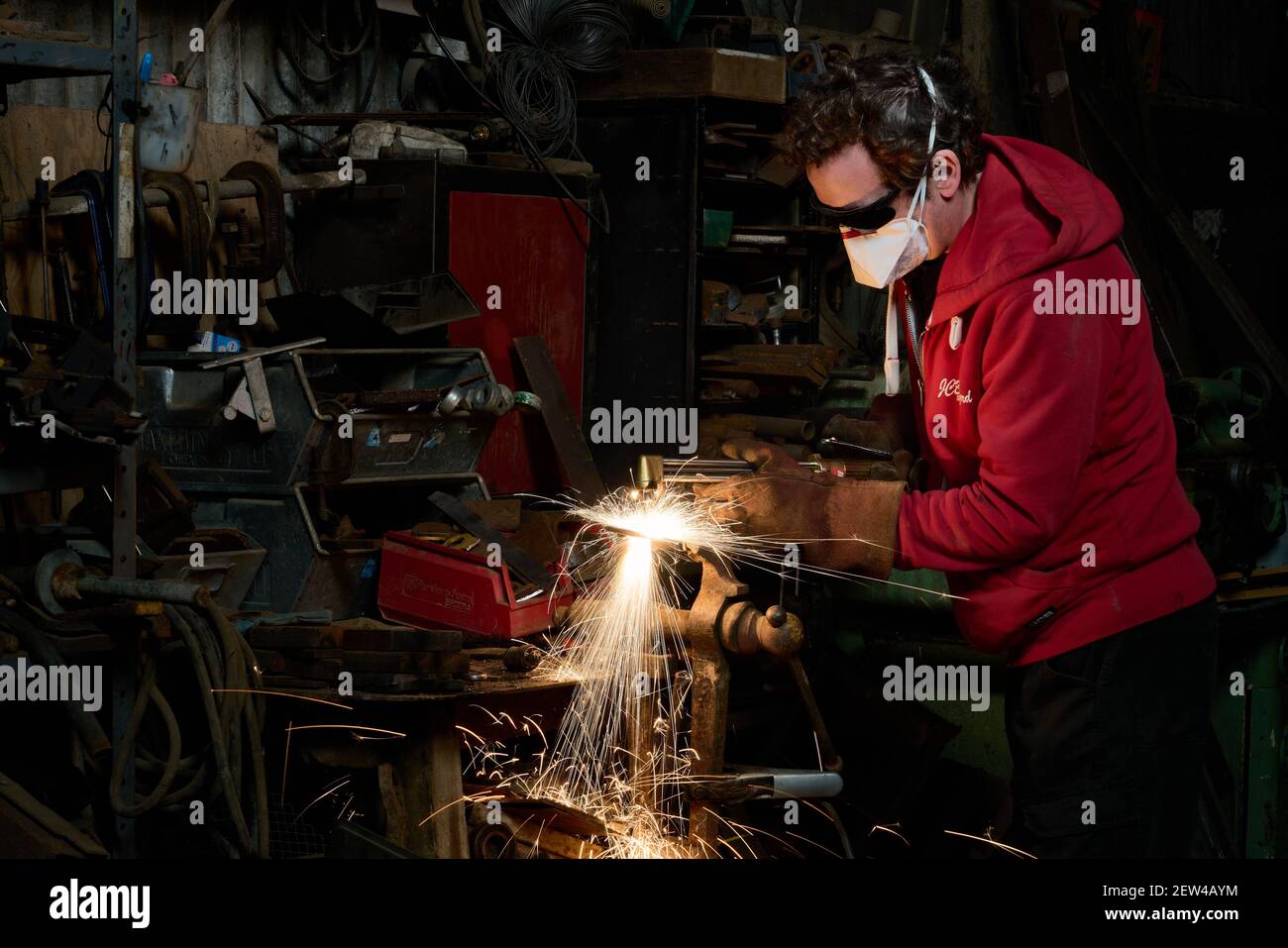 Métal de coupe caucasien mâle avec un chalumeau oxy-acétylène dans un Atelier de ferme portant un masque FFP3 et une protection oculaire sombre Banque D'Images