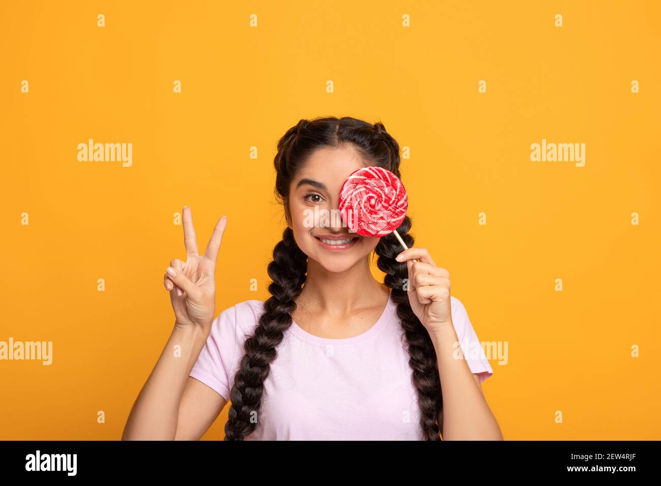 Femme indienne tenant un lollipop, couvrant l'œil, montrant le signe de la paix Banque D'Images