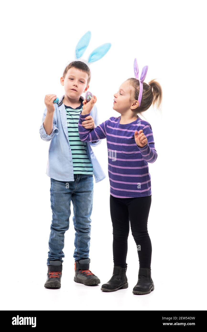 Joyeux petits enfants joueurs frères et sœurs jouant le jeu des oeufs de taraudage avec des oeufs de Pâques peints. Corps entier isolé sur fond blanc. Banque D'Images