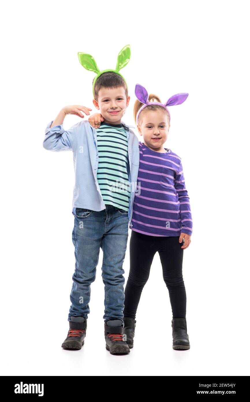 Petite fille mignonne embrassant un frère plus âgé portant des oreilles de lapin de Pâques. Corps entier isolé sur fond blanc. Banque D'Images