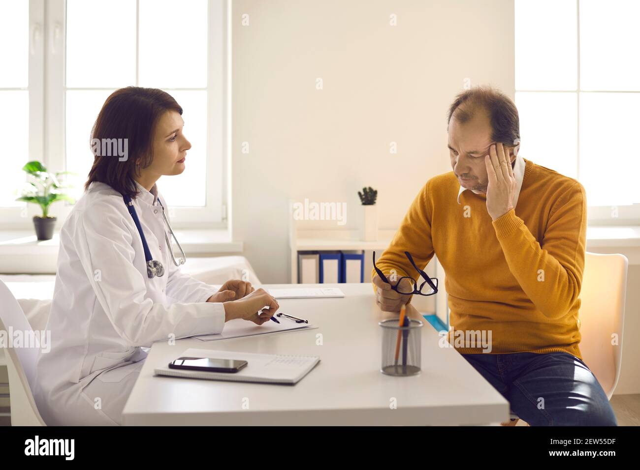 Médecin à l'écoute d'un patient de sexe masculin se plaignant de maux de tête, de stress et de fatigue Banque D'Images