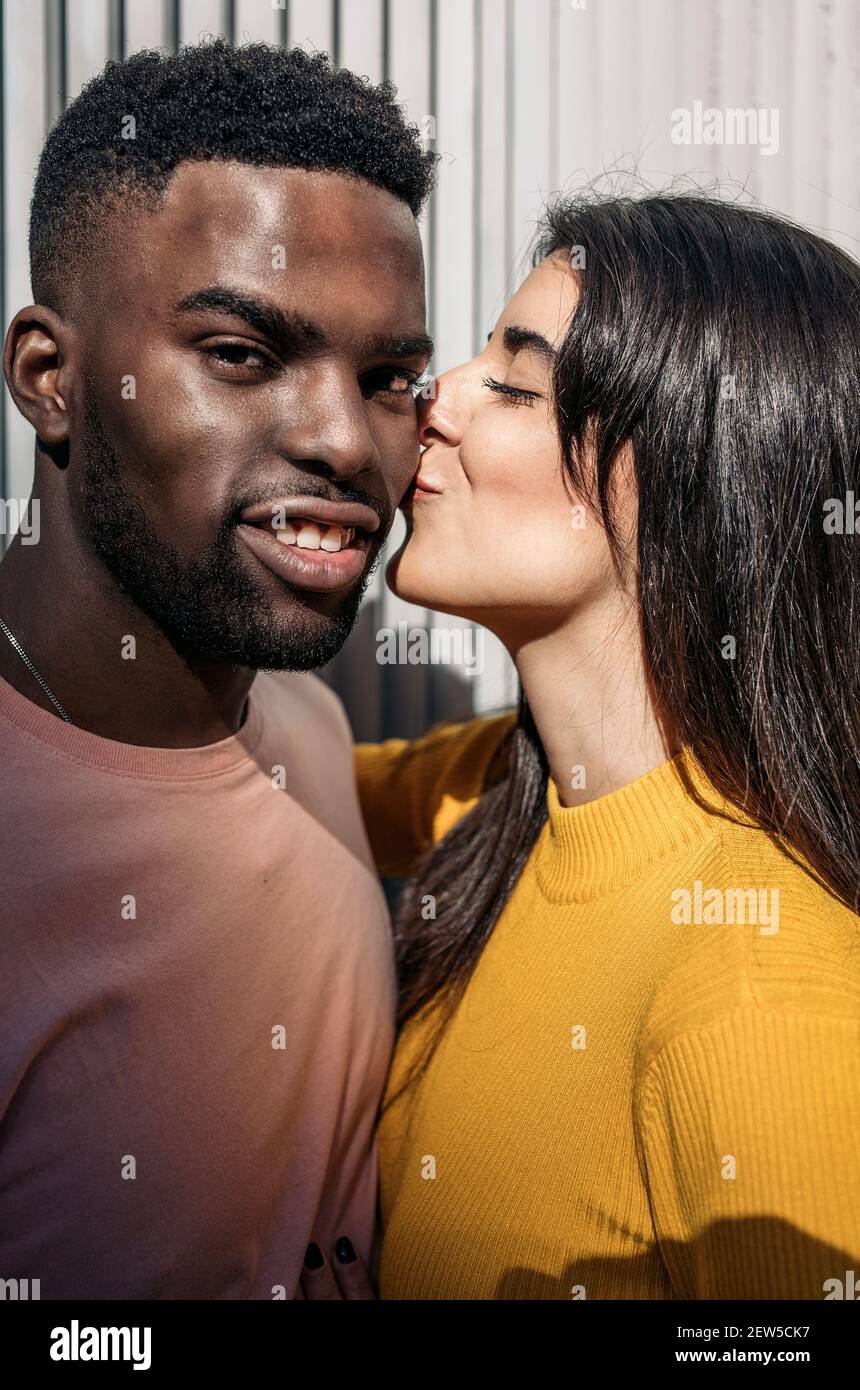 Belle femme se déplace pour embrasser le visage d'un frais homme noir regardant la caméra Banque D'Images